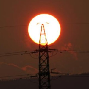 a photo of the setting sun viewed through a tall electricity pylon